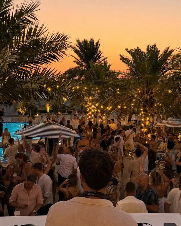 A DJ at the decks by the pool at dusk, seen from behind. AI-generated image.